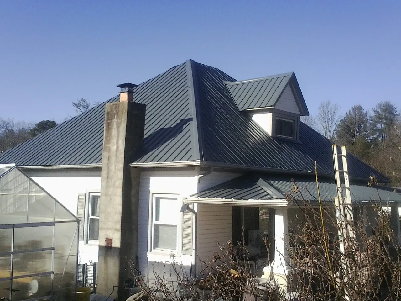 Dark blue standing seam metal roof on a white farmhouse with dormer — Slate & Tile Roof Repair by Roofing Brothers in Evensville