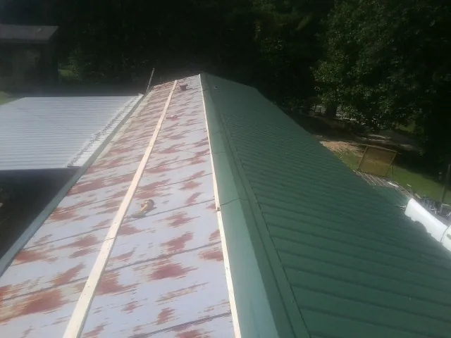 Old rusted panels beside newly installed green metal roofing — Wind Damage Roof Repair by Roofing Brothers in Evensville