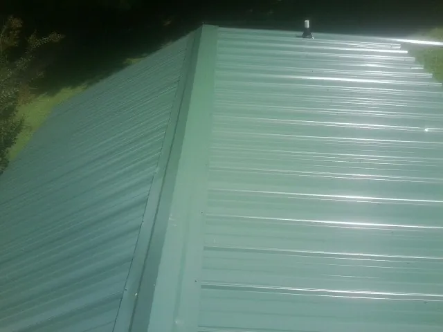 New green metal panels meeting at the ridge of a roof — Flat Roof Repair work by our crew in Evensville