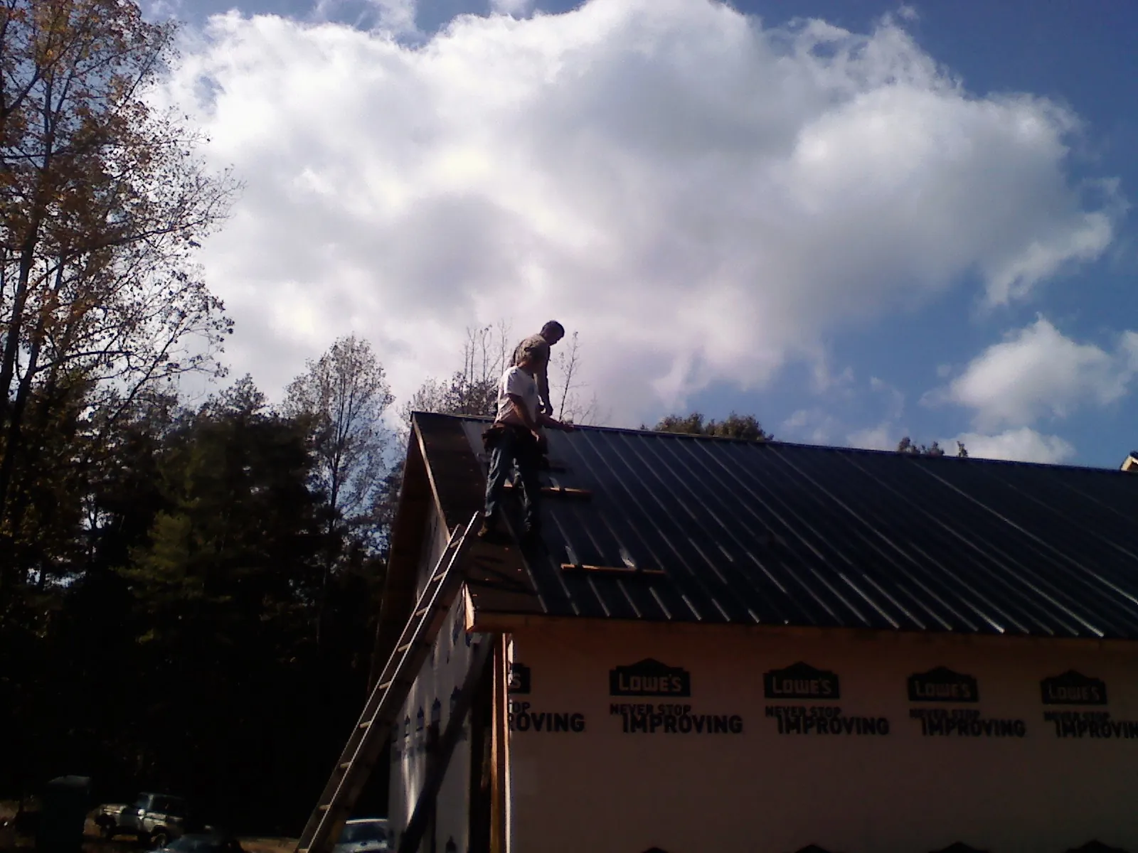 Roofer fastening dark metal panels high against a cloudy sky, from a Roof Inspection job in Evensville