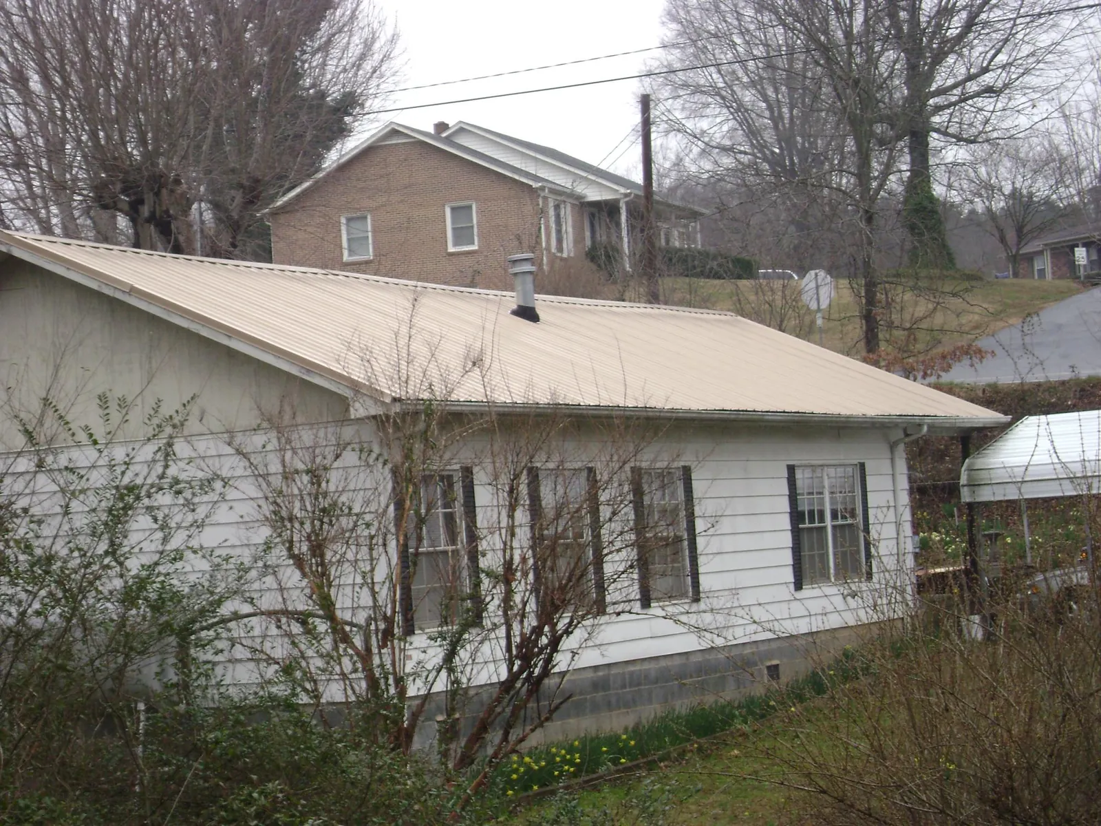 Tan metal roof on a white sided house set into a hillside — Commercial Roofing by Roofing Brothers in Evensville