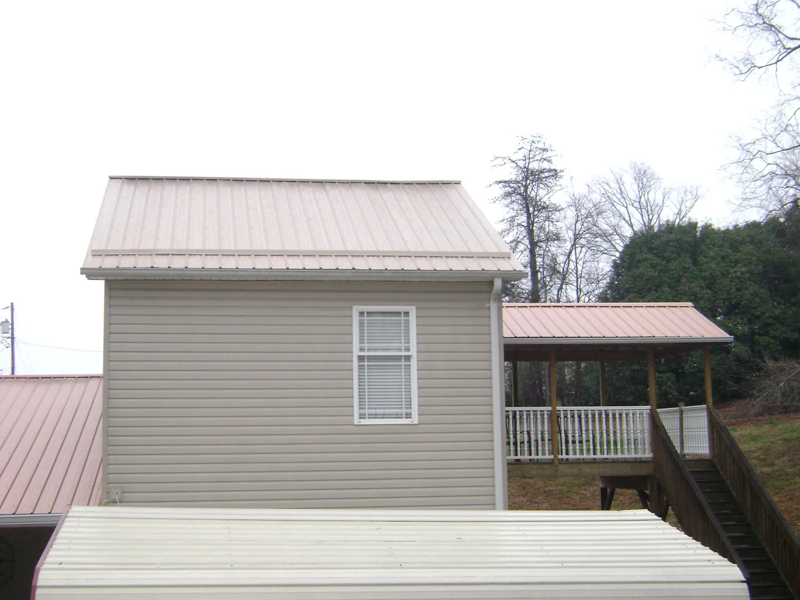 Tan metal roofs on a two story addition and attached porch, from a Roof Replacement job in Evensville